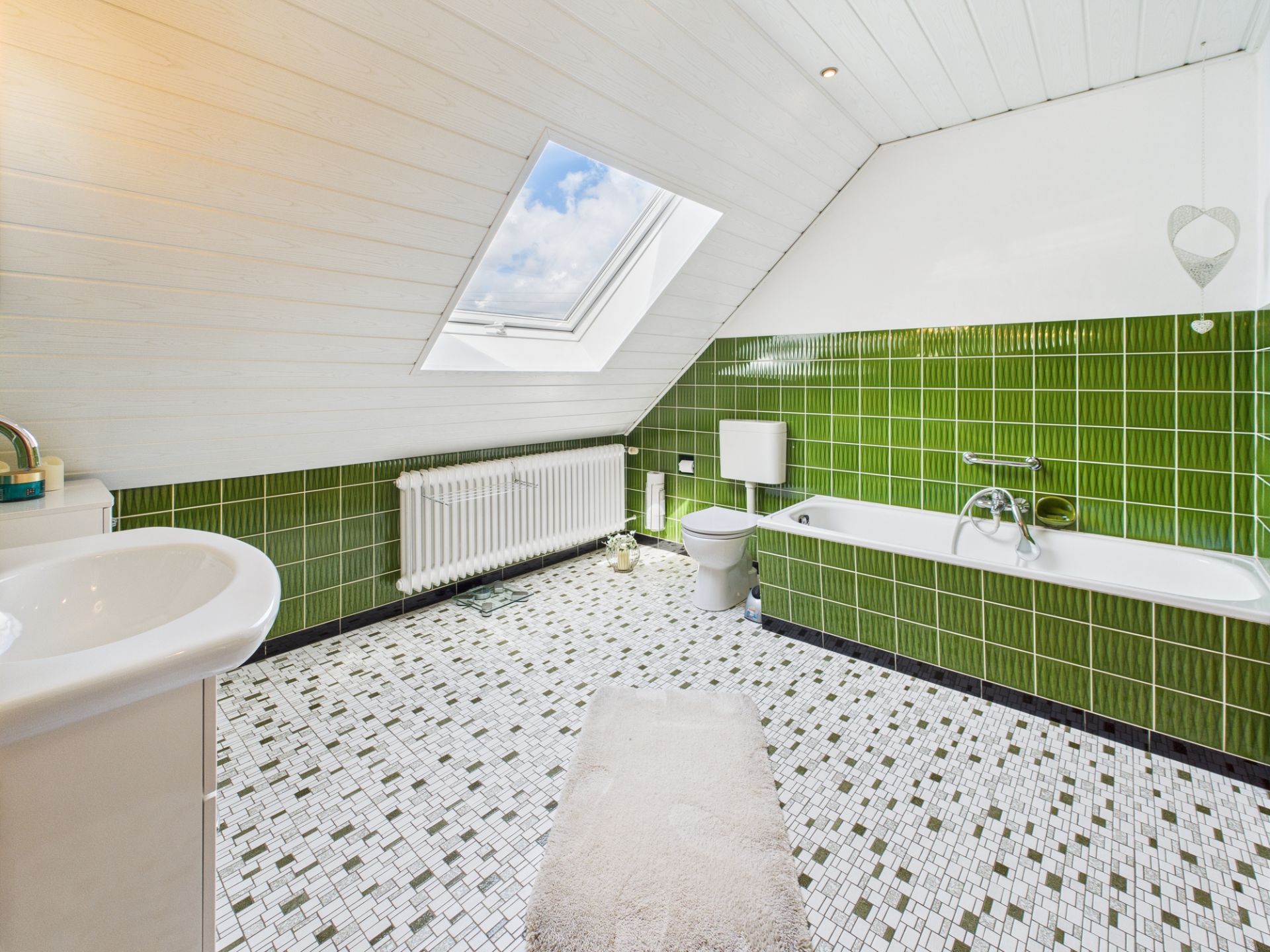 Helles Badezimmer mit grünen Wandfliesen, Badewanne, WC und Dachfenster.