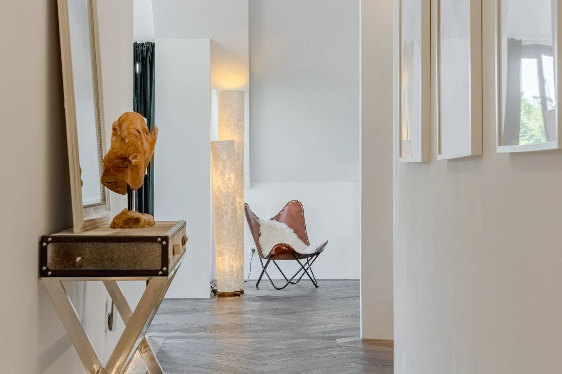 Flur mit Konsole, Holzskulptur, Bildern, Stehlampe und braunem Stuhl mit Fell.