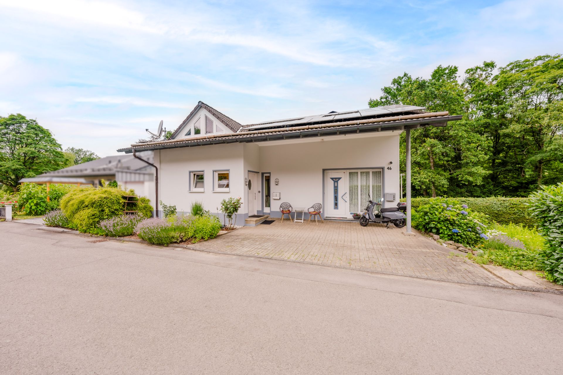 Modernes Einfamilienhaus mit Terrasse, Gartenmöbeln und Kinderwagen vor dem Eingang.