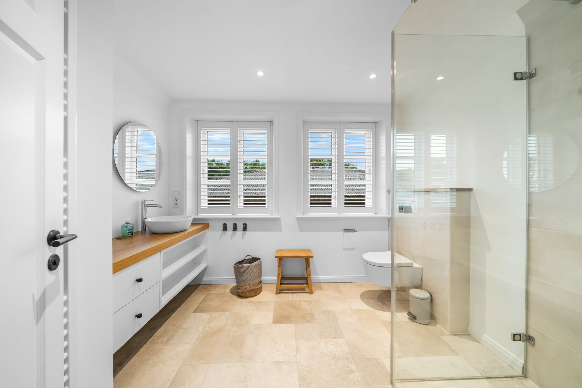 Modernes Badezimmer mit großer Dusche, Doppelwaschbecken, Fenster und hellen Fliesen.