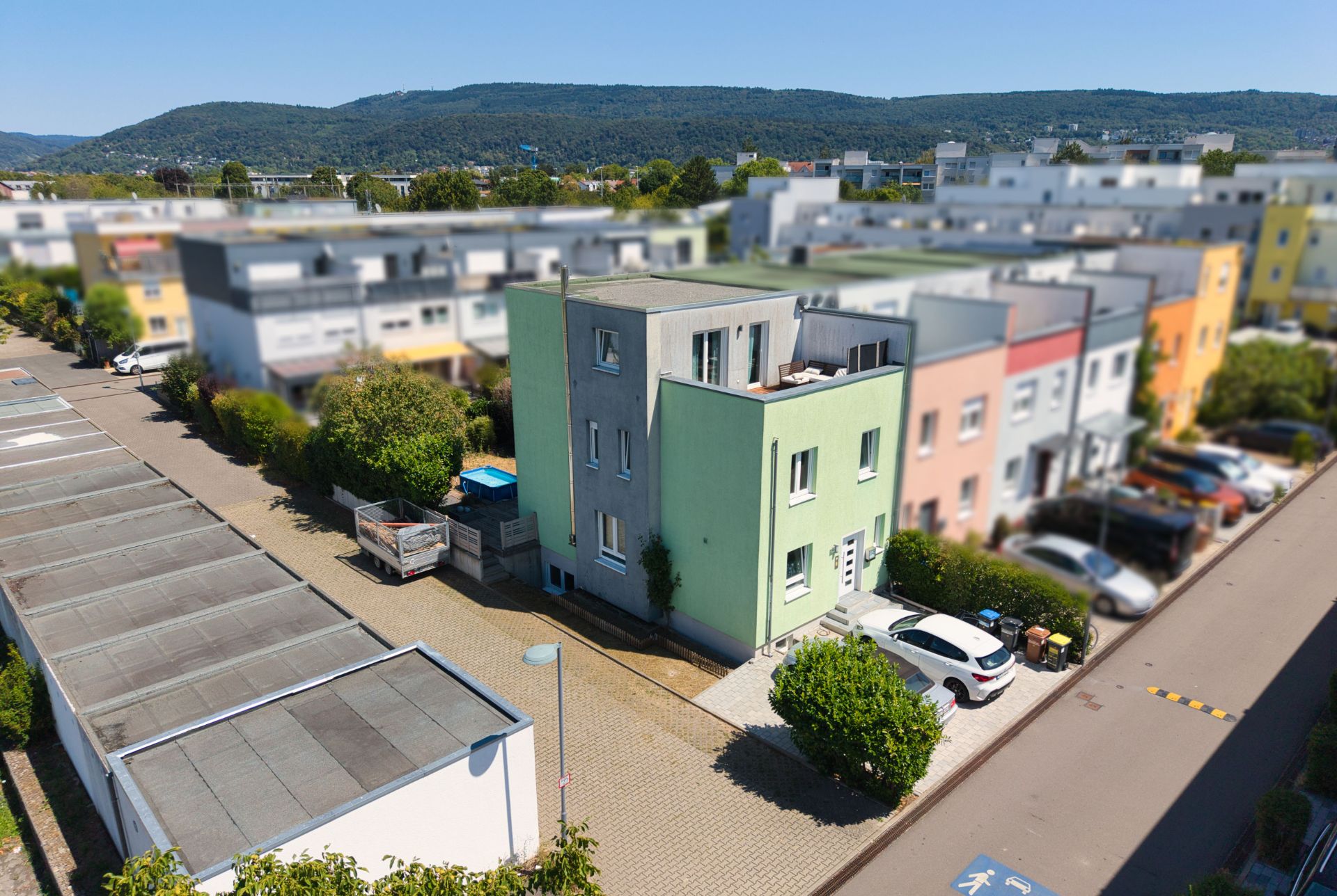 Grünes, modernes Wohnhaus mit drei Etagen und davor parkenden Autos in einer Wohnsiedlung.