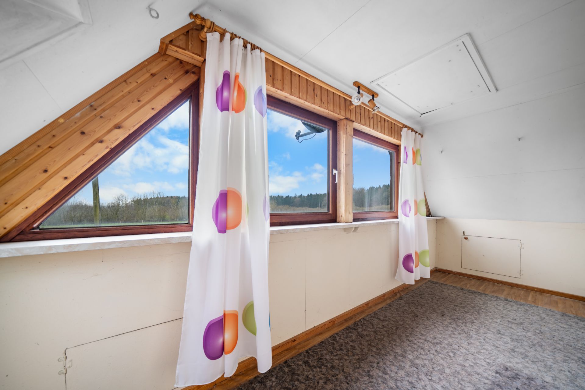 Zimmer mit großem Fenster, bunten Vorhängen und Blick ins Grüne.
