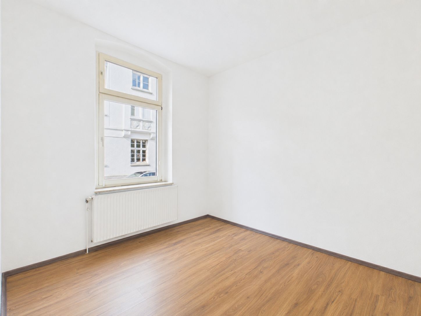 Leerer, heller Raum mit weißer Wand, Holzfußboden, Fenster und Heizkörper.