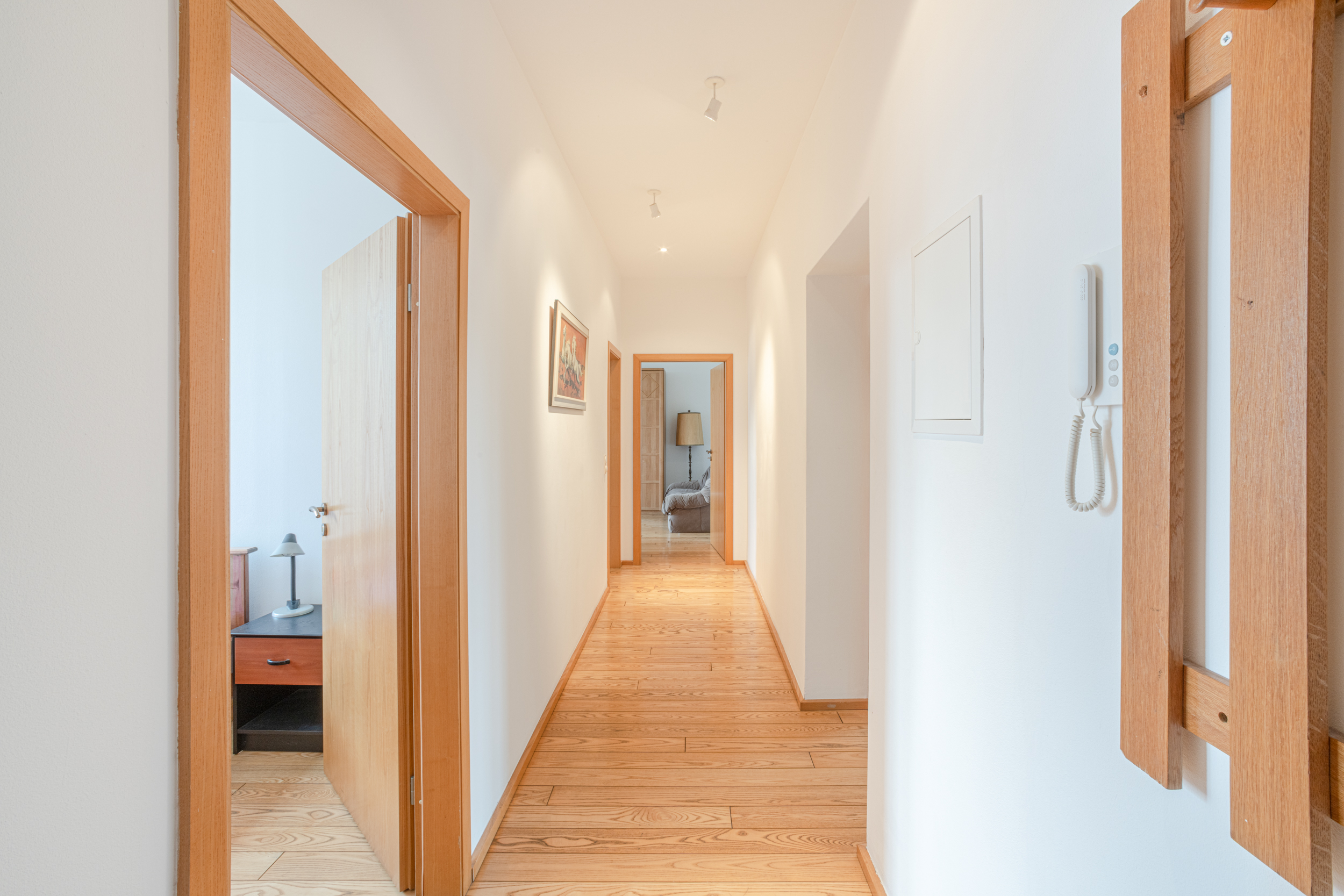 Heller Flur mit Holzboden, weißen Wänden und mehreren offenen Türen.