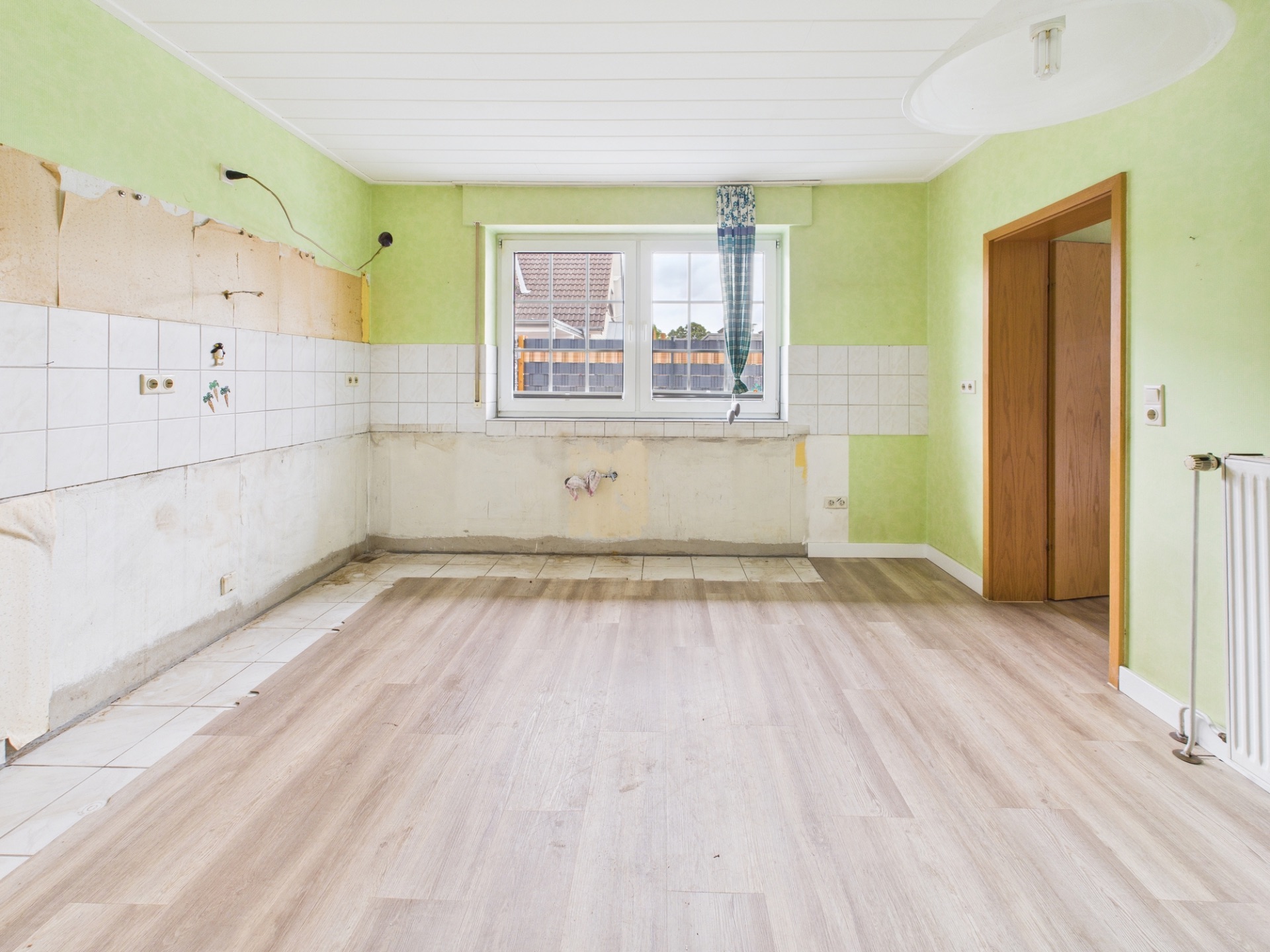 Leerer Raum mit grün gestrichenen Wänden, Fenster und offenem Durchgang.