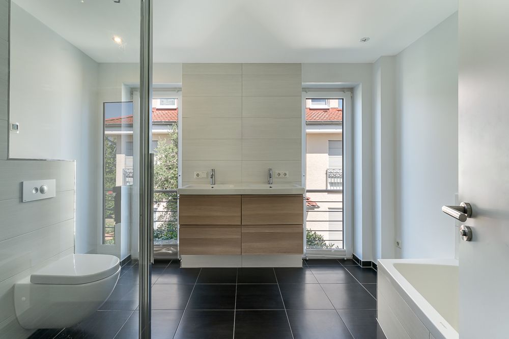 Modernes Badezimmer mit Doppelwaschbecken, Toilette, Badewanne und großen Fenstern.