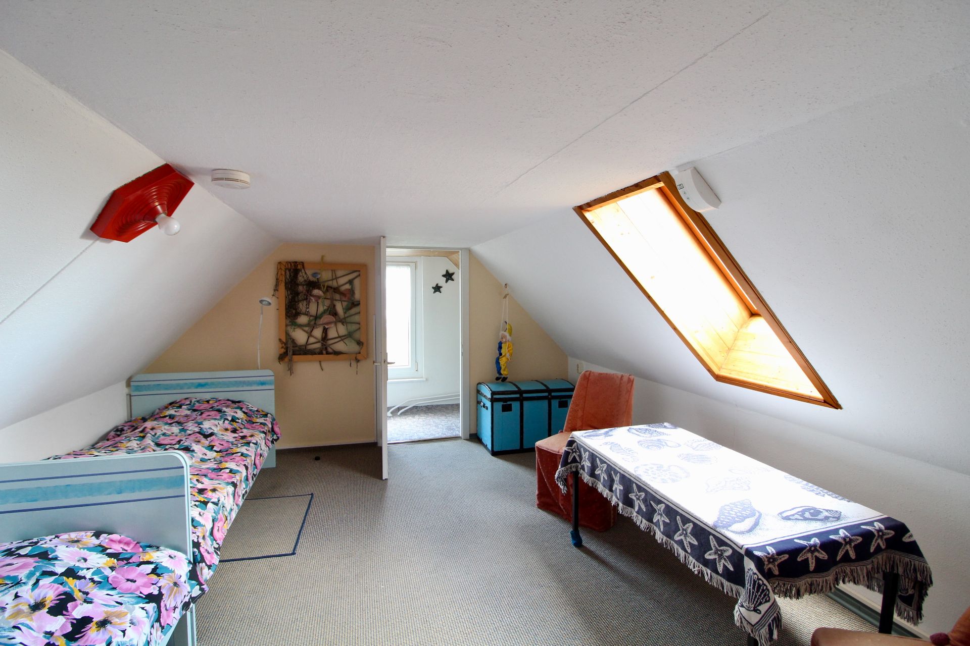 Dachzimmer mit zwei Betten, Tisch, Stuhl und Dachfenster.