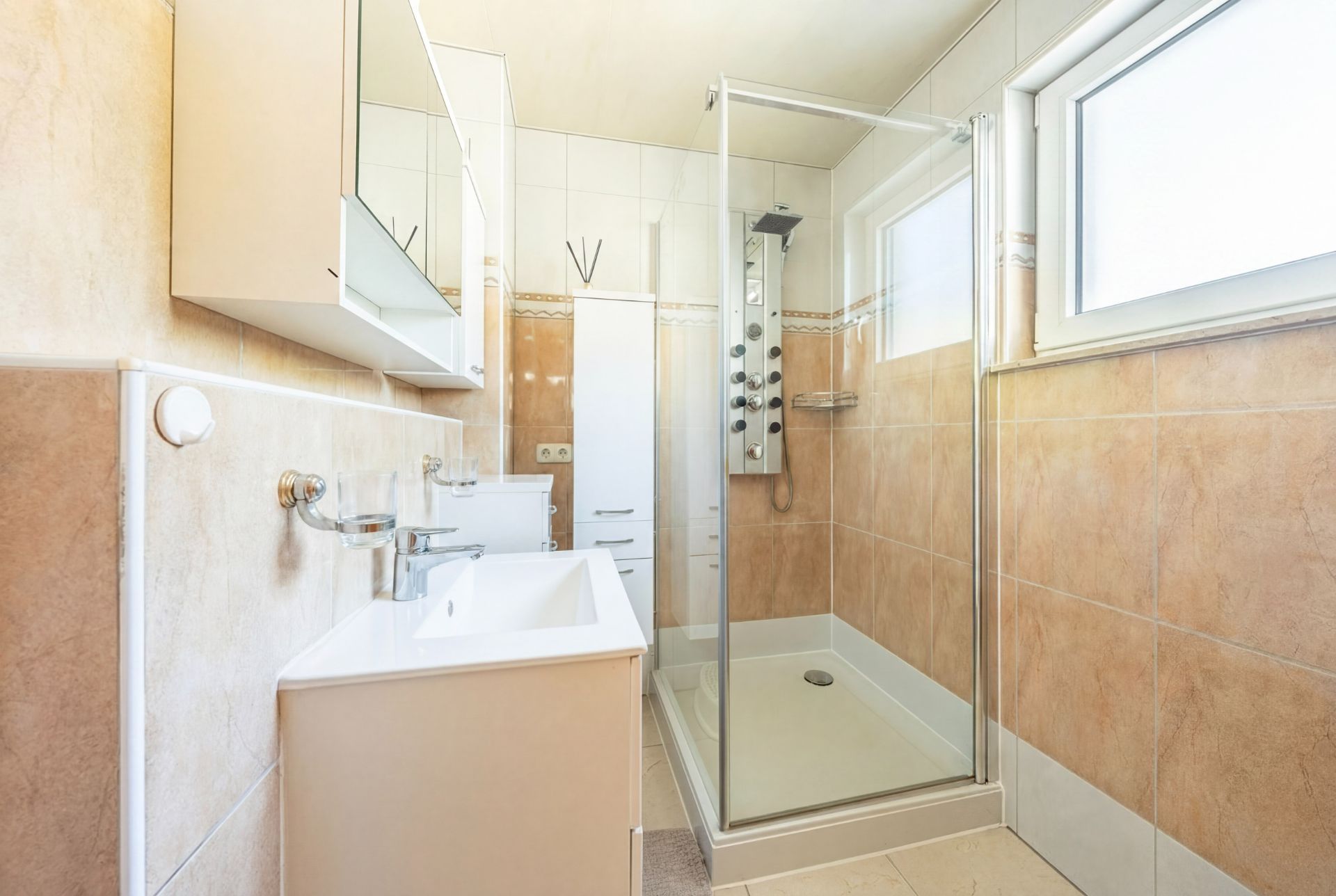 Helles Badezimmer mit Waschbecken, Spiegel, großer Dusche und Fenster.