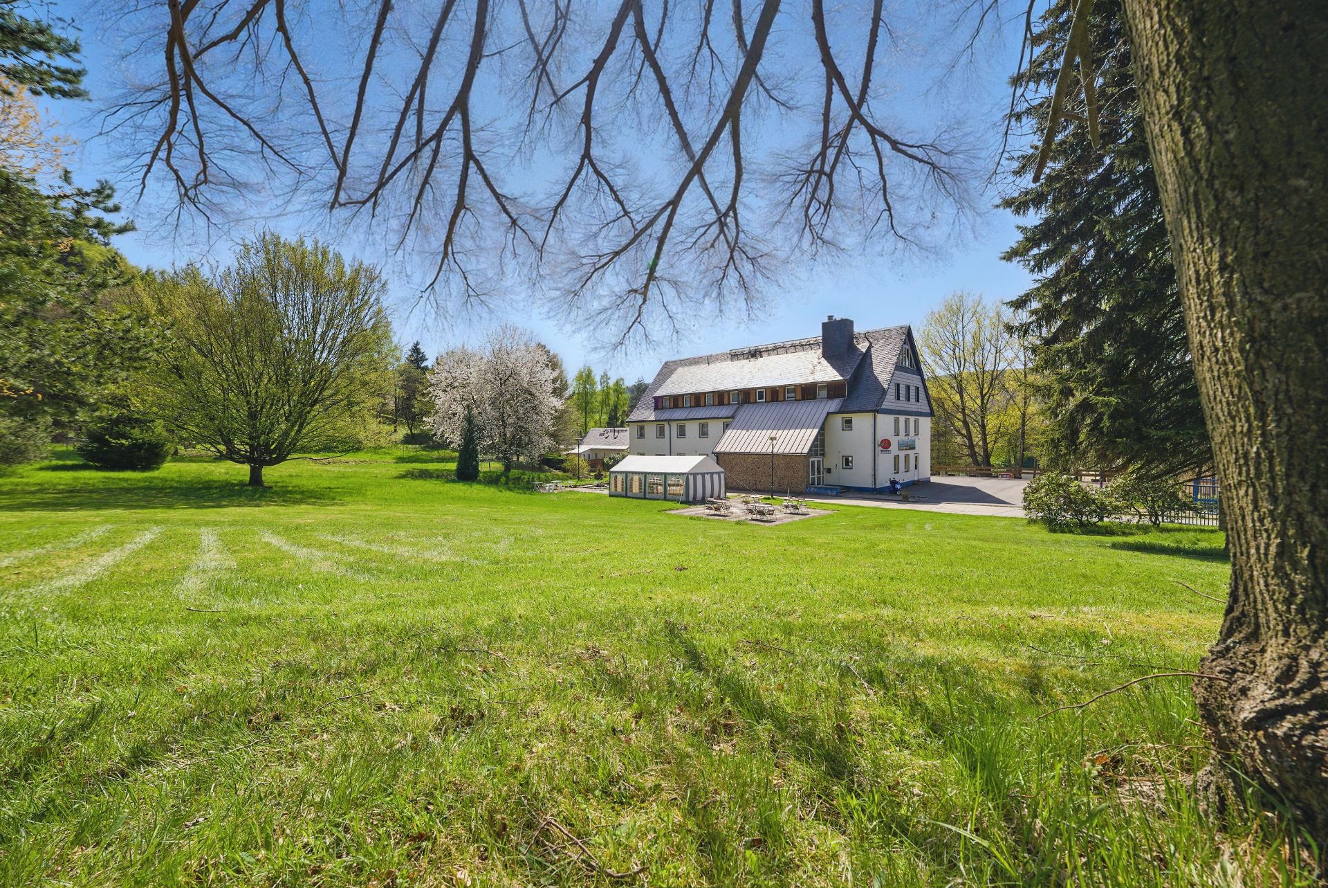 Großes Wohnhaus mit Garten, Bäumen und Rasenfläche bei sonnigem Wetter.
