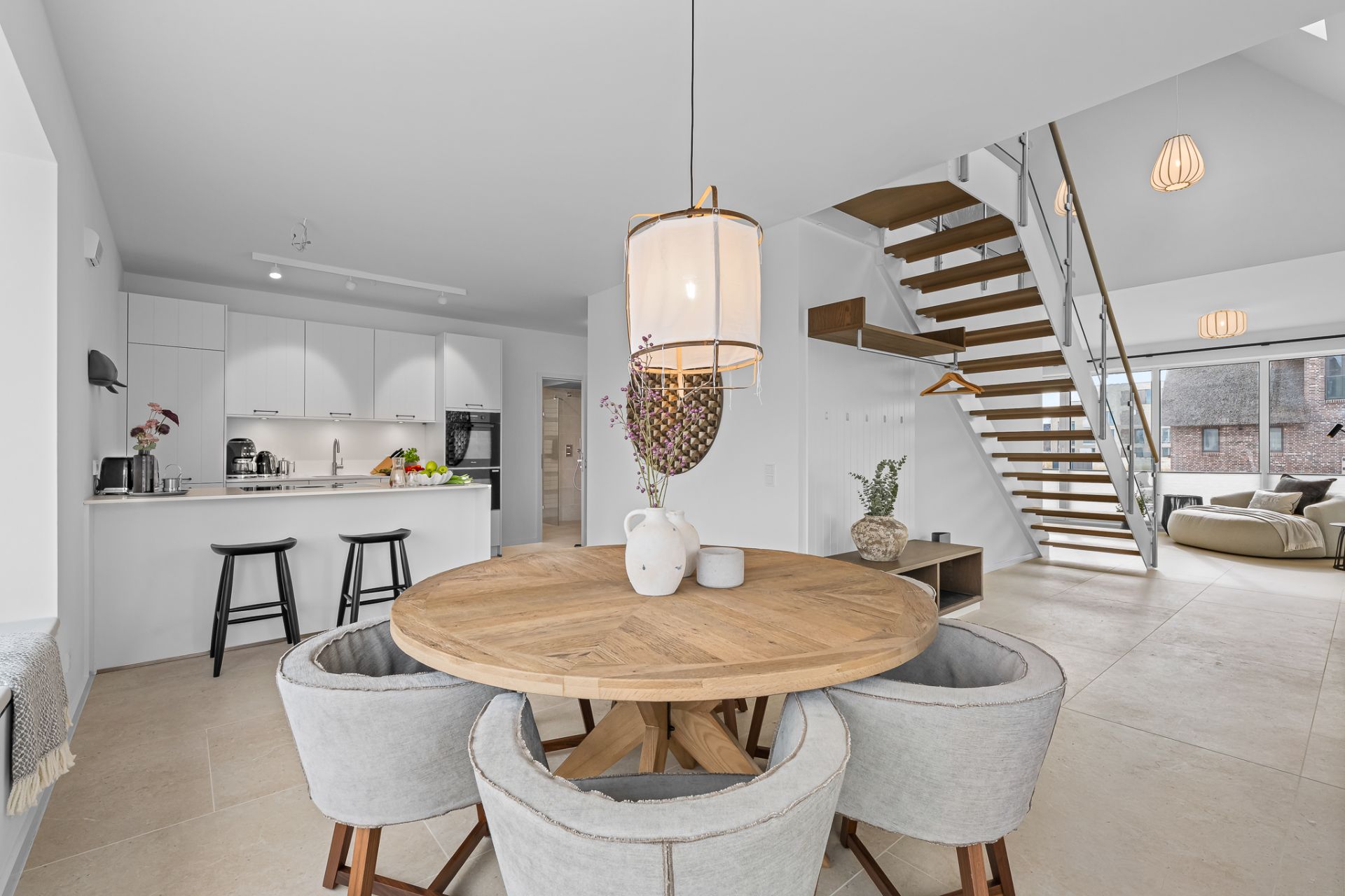 Helles Wohnzimmer mit offener Küche, rundem Esstisch und moderner Holztreppe.