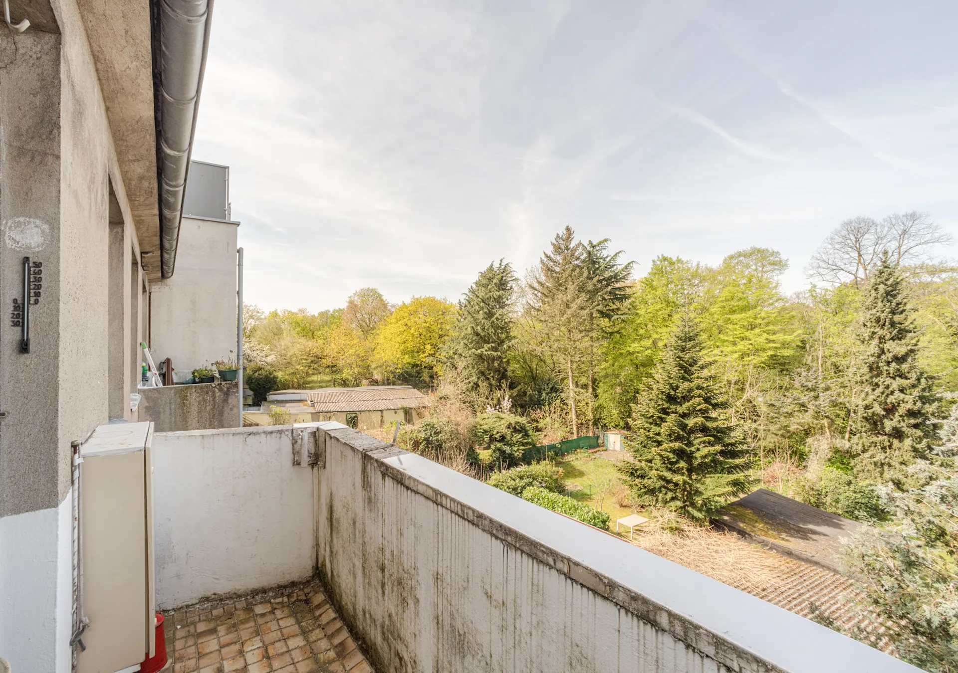 Balkon mit Blick auf grüne Bäume und einen Garten, Gebäude am linken Rand sichtbar.