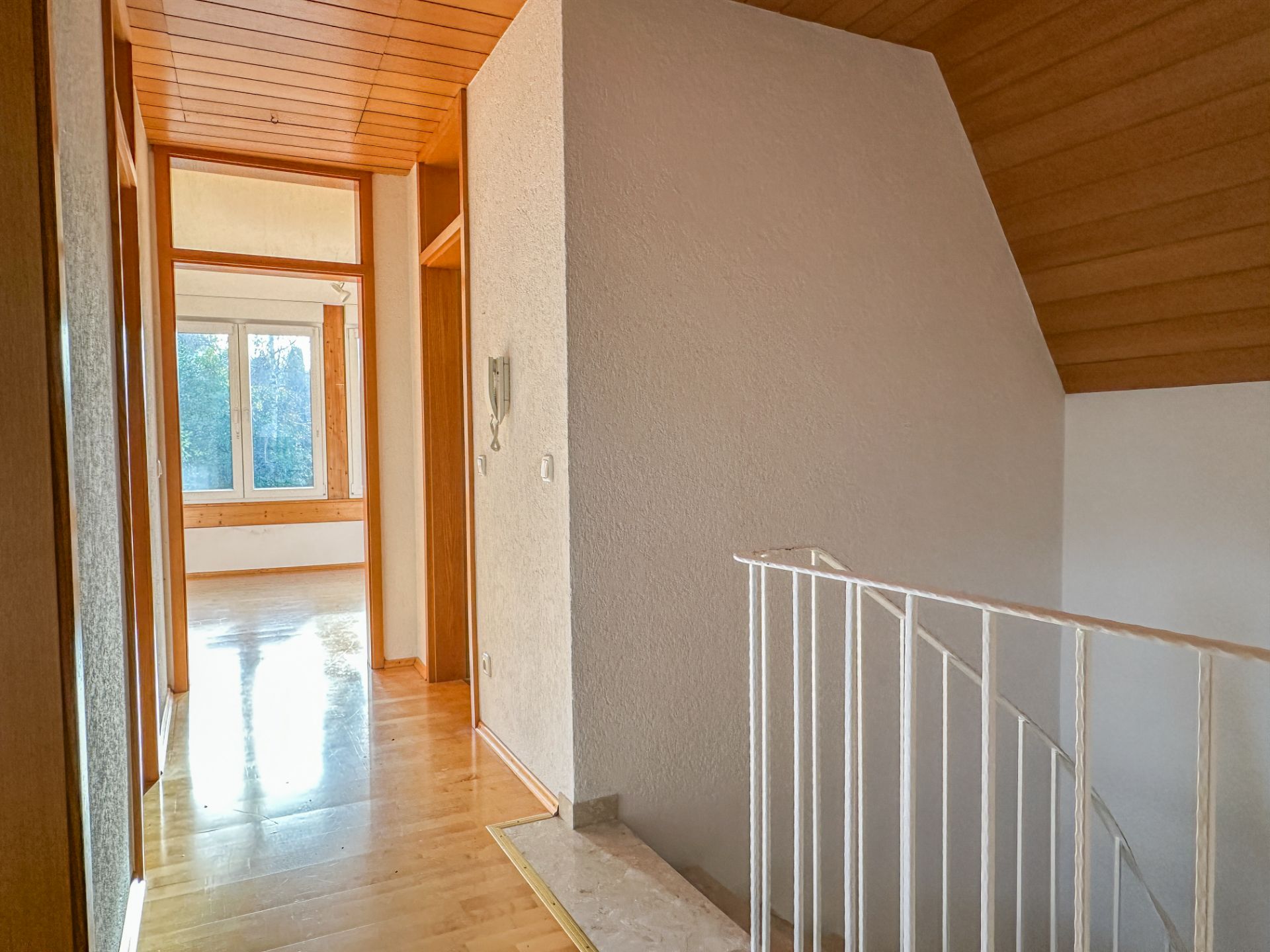 Heller Flur mit Holzdecke, Treppengeländer und großem Fenster im Hintergrund.