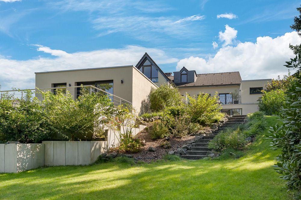 Modernes Wohnhaus mit Garten, Terrasse und Treppe, umgeben von grünen Pflanzen.