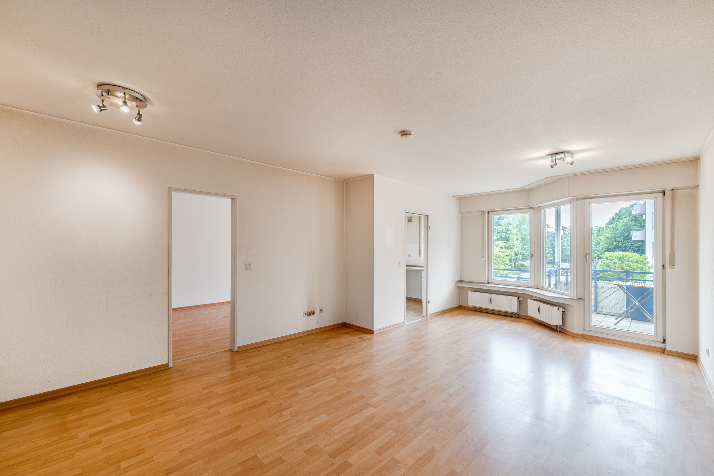 Helles Wohnzimmer mit Parkettboden, großen Fenstern und Zugang zu einem Balkon.