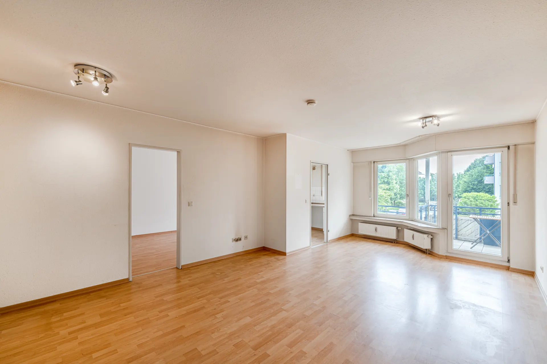 Helles Wohnzimmer mit Parkettboden, großen Fenstern und Zugang zu einem Balkon.
