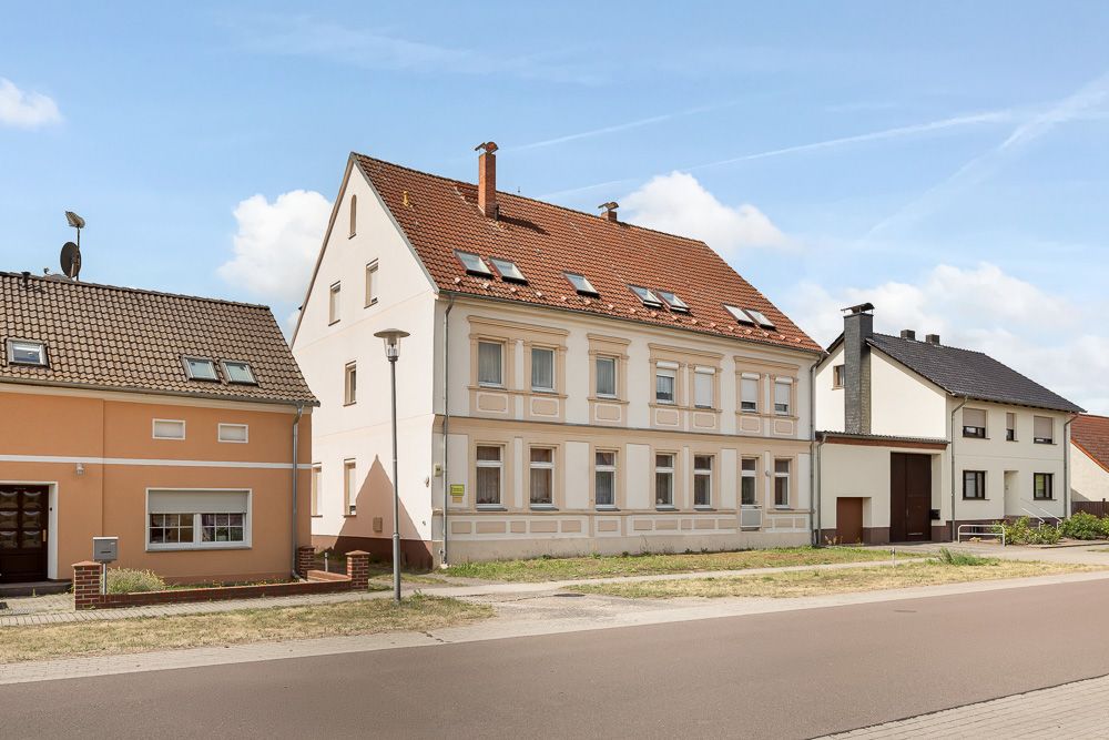 Mehrfamilienhaus mit rotem Dach und mehreren Fenstern an einer ruhigen Straße.