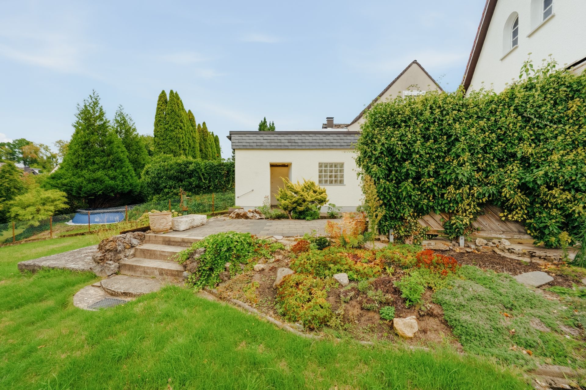 Garten mit Steinweg, Stufen, Terrasse und Pflanzen neben einem Wohnhaus.