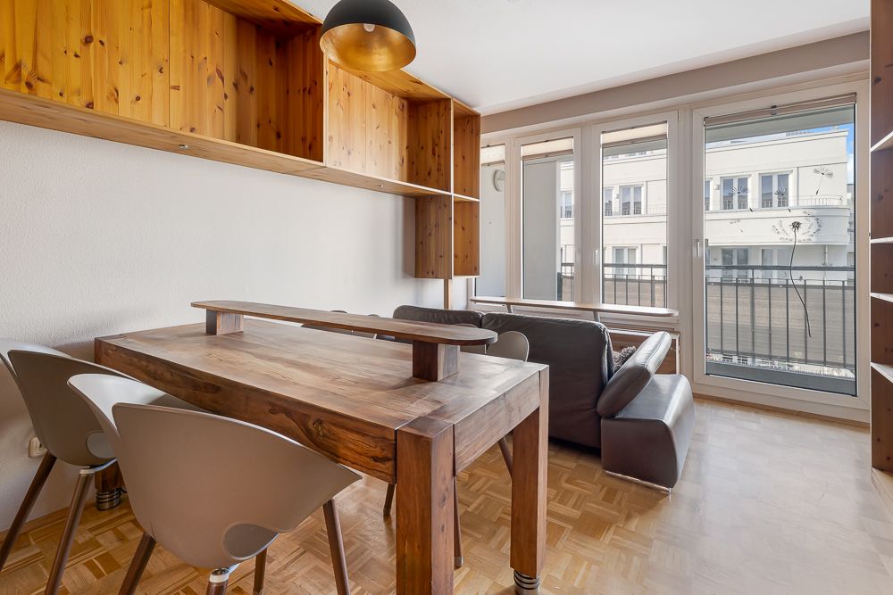 Wohnzimmer mit Holztisch, Stühlen, Sofa und großen Fenstern mit Blick nach draußen.