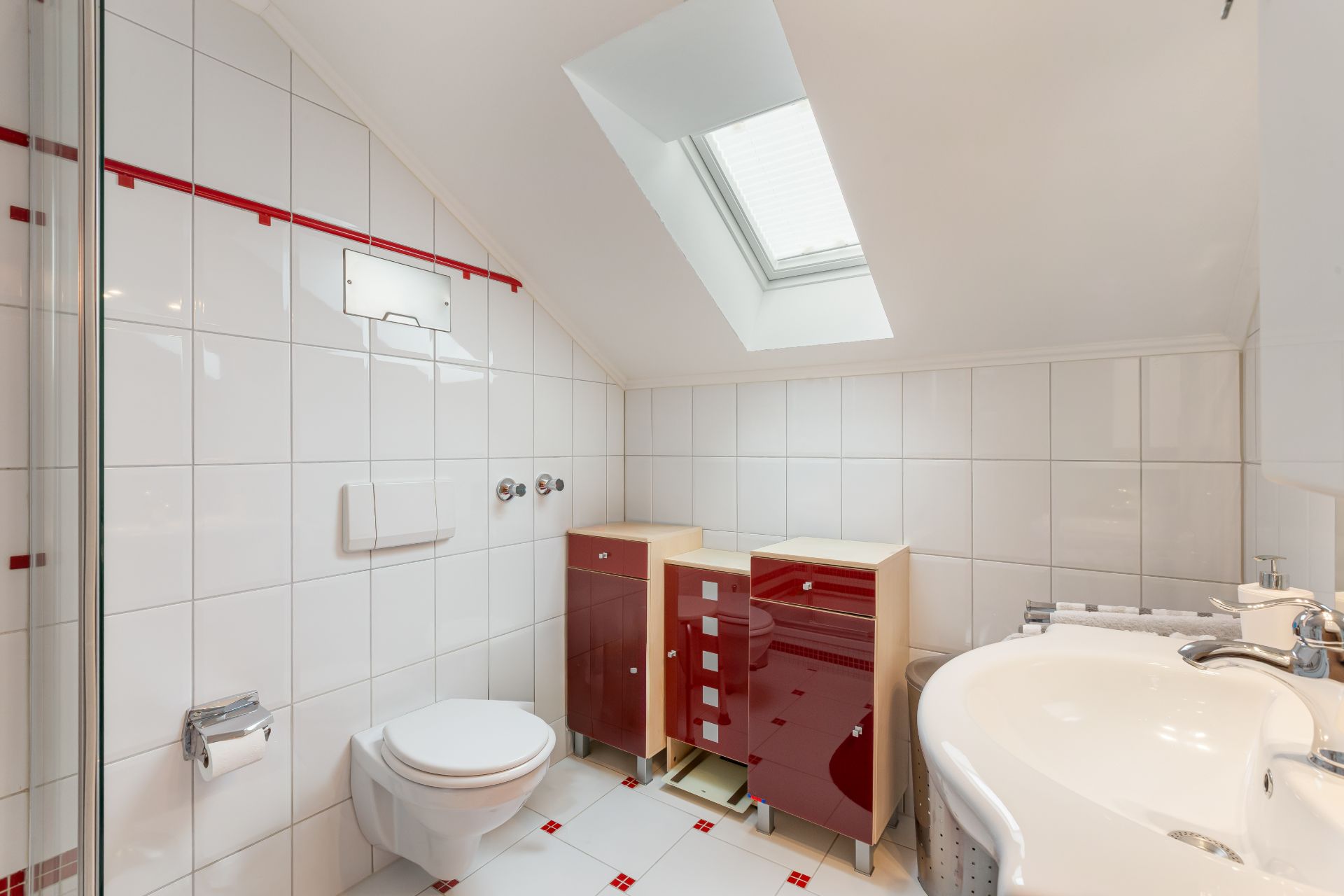 Modernes Bad mit weißen Fliesen, Dachfenster, Hänge-WC und roten Schränken.