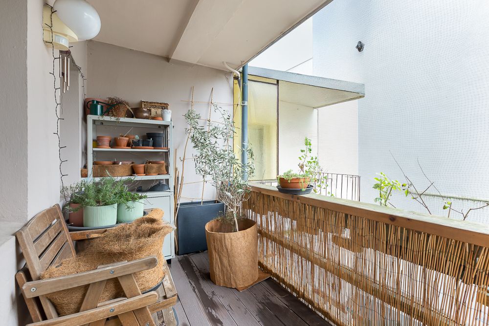 Balkon mit Holzstuhl, Regal voller Blumentöpfe und Pflanzen an der Brüstung.
