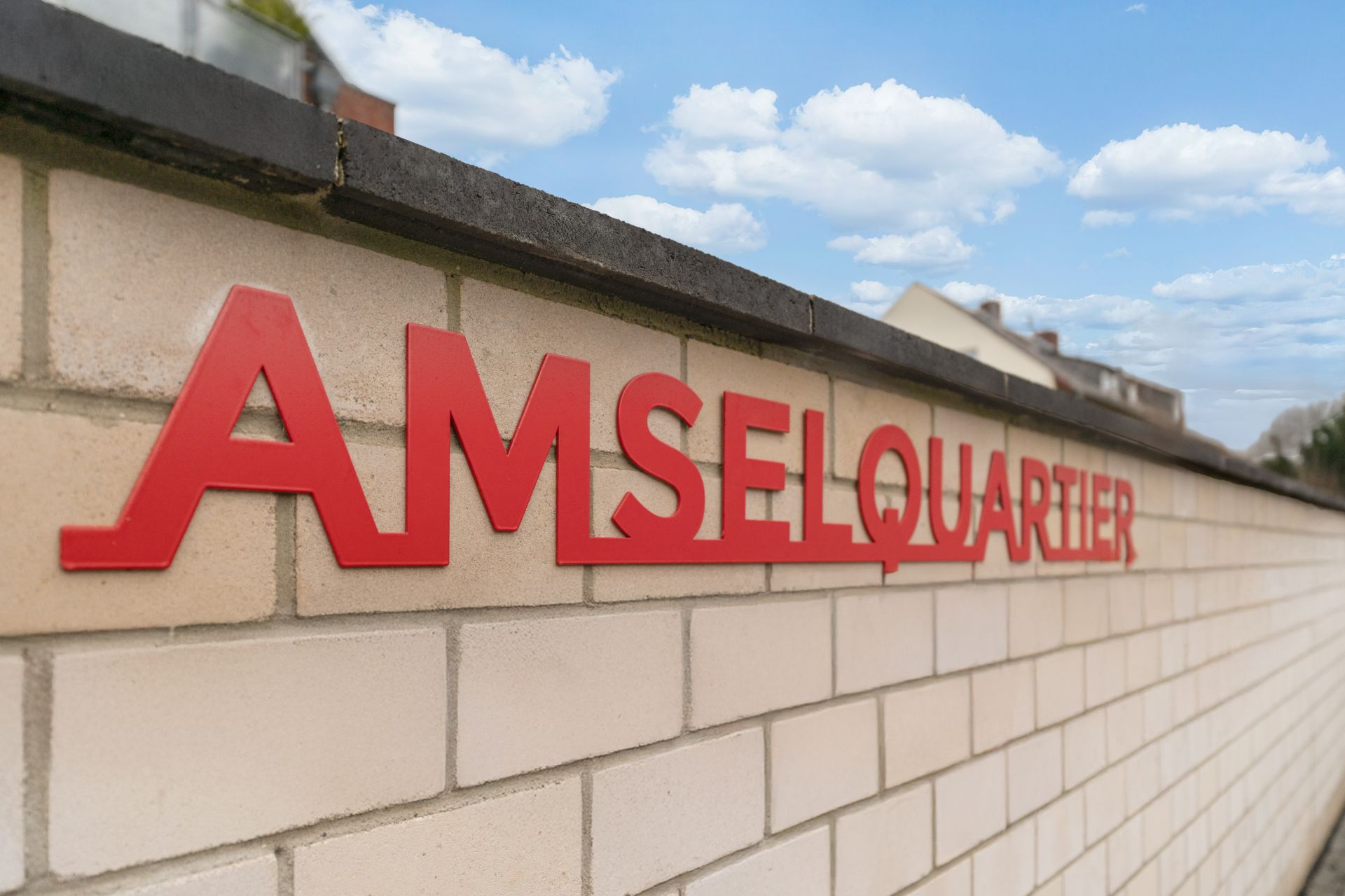 Rote Buchstaben mit dem Schriftzug 'AMSELQUARTIER' auf einer hellen Backsteinmauer.
