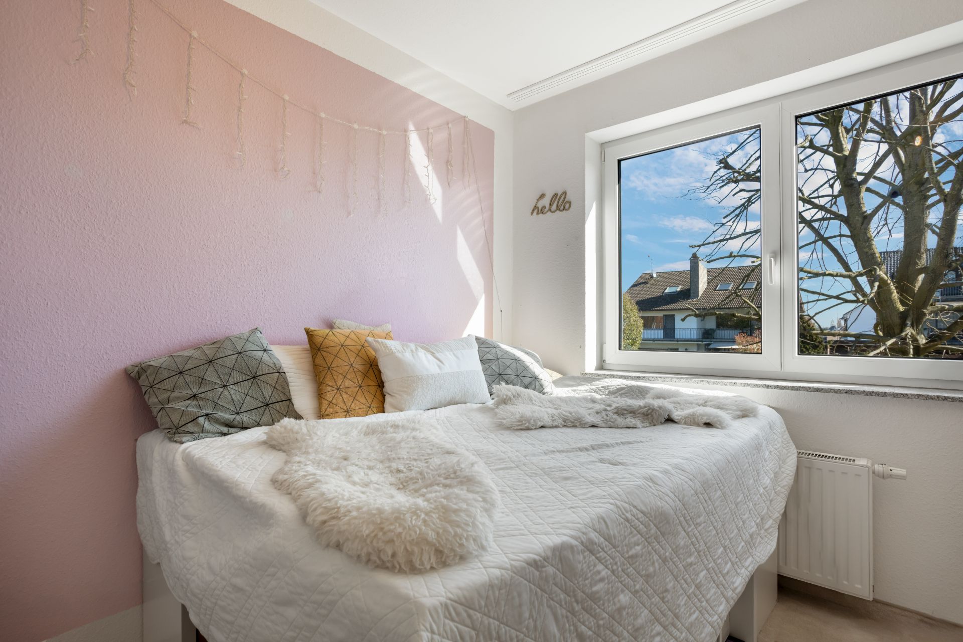 Helles Schlafzimmer mit großem Bett, Dekokissen und Fenster mit Blick nach draußen.