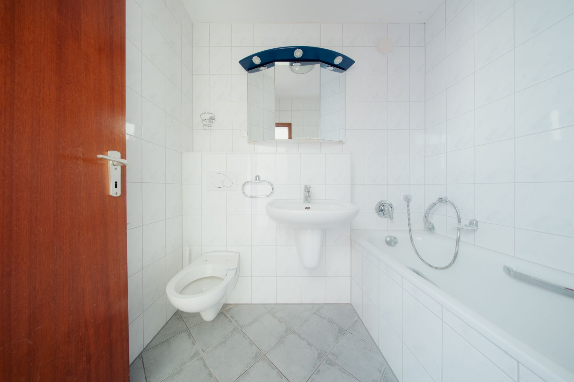 Helles Badezimmer mit Badewanne, Wand-WC, Waschbecken und Spiegel.