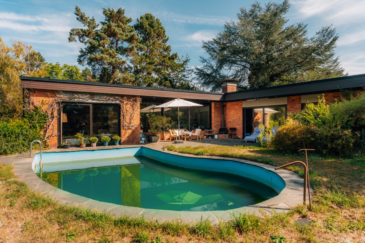 Backsteinbungalow mit großem Fenster, Terrasse und kleinem Pool im Garten.
