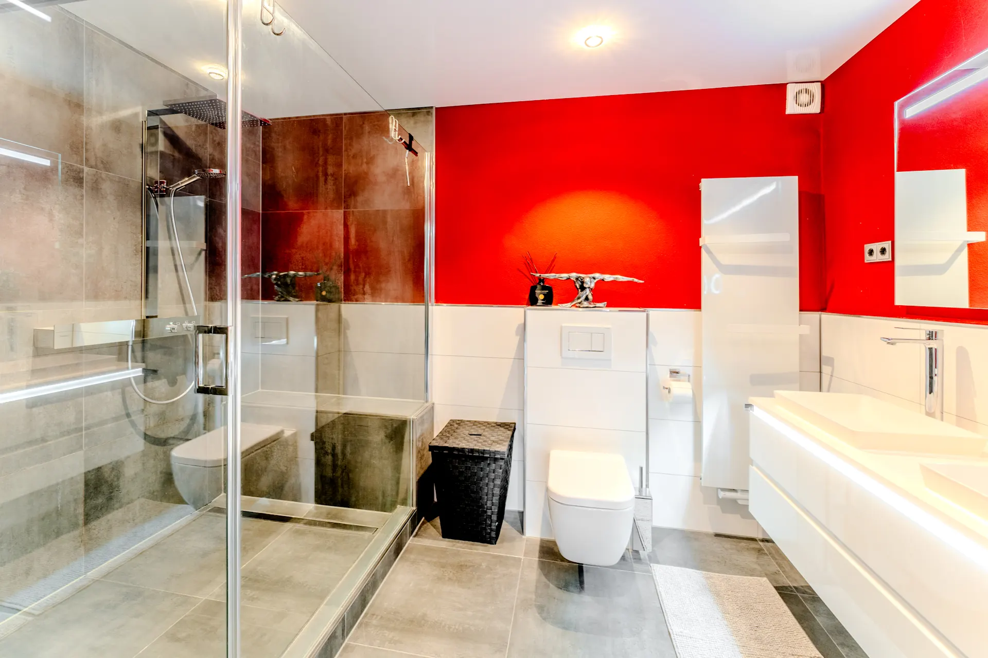 Modernes Badezimmer mit roter Wand, Dusche, WC, Waschbecken und großem Spiegel.