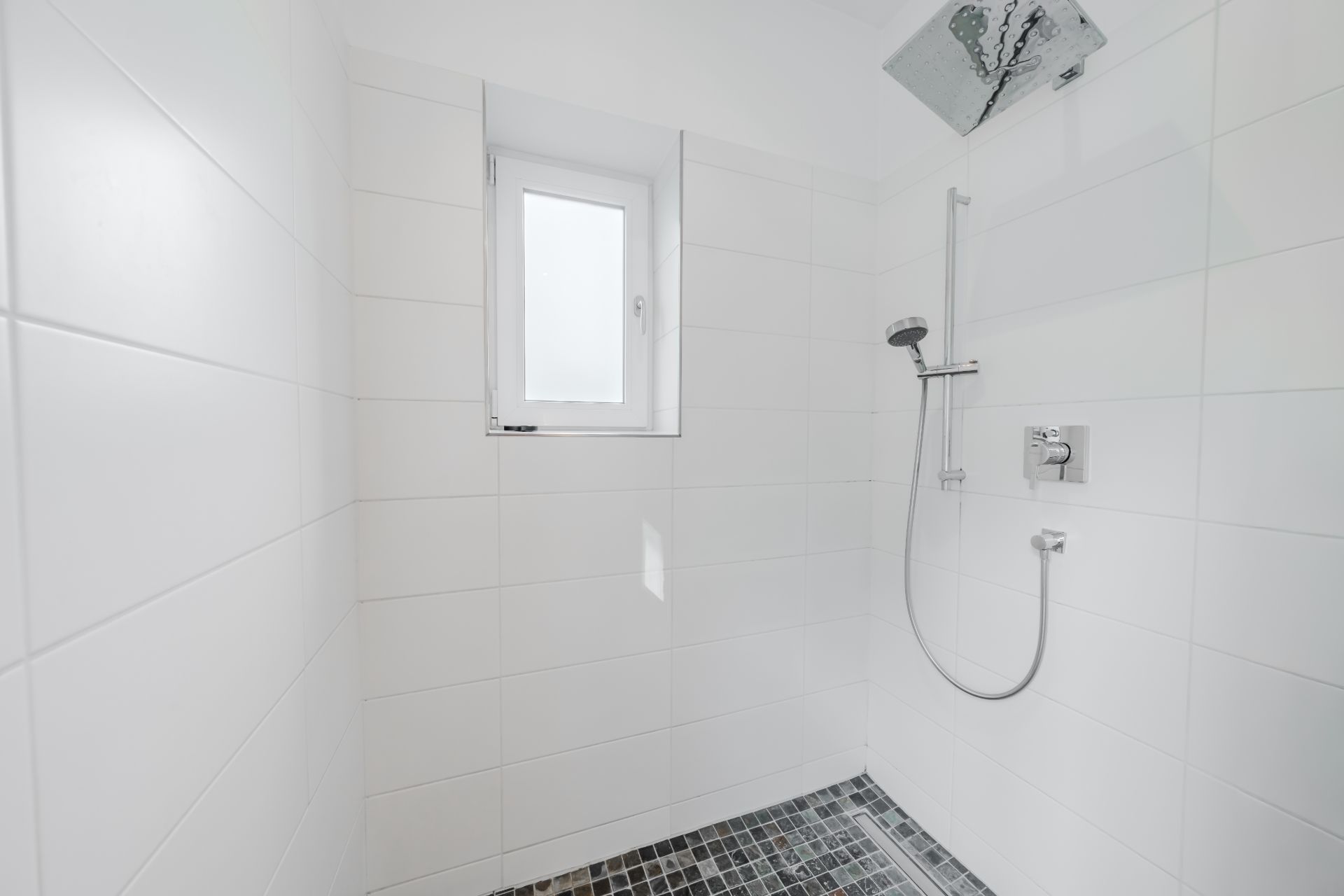 Helle, geflieste Dusche mit Fenster, Duschkopf und Handbrause.