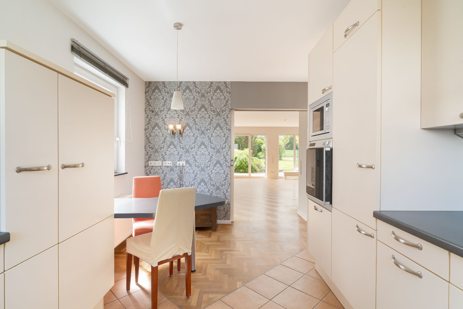 Helle Küche mit Esstisch, Stühlen und Blick in ein großes Wohnzimmer mit Parkettboden.