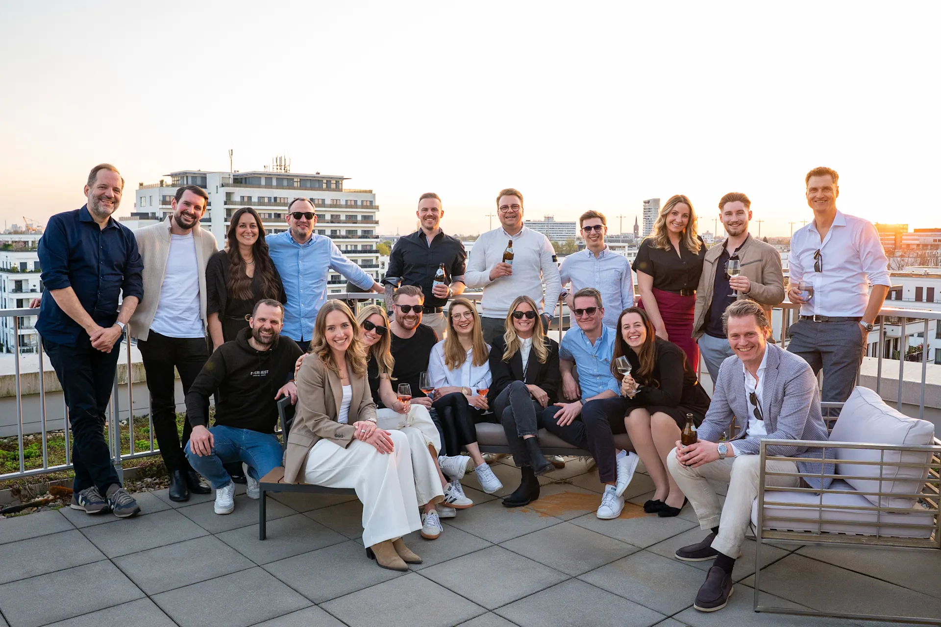 Eine Gruppe von Menschen sitzt und steht auf einer Dachterrasse bei Sonnenuntergang.