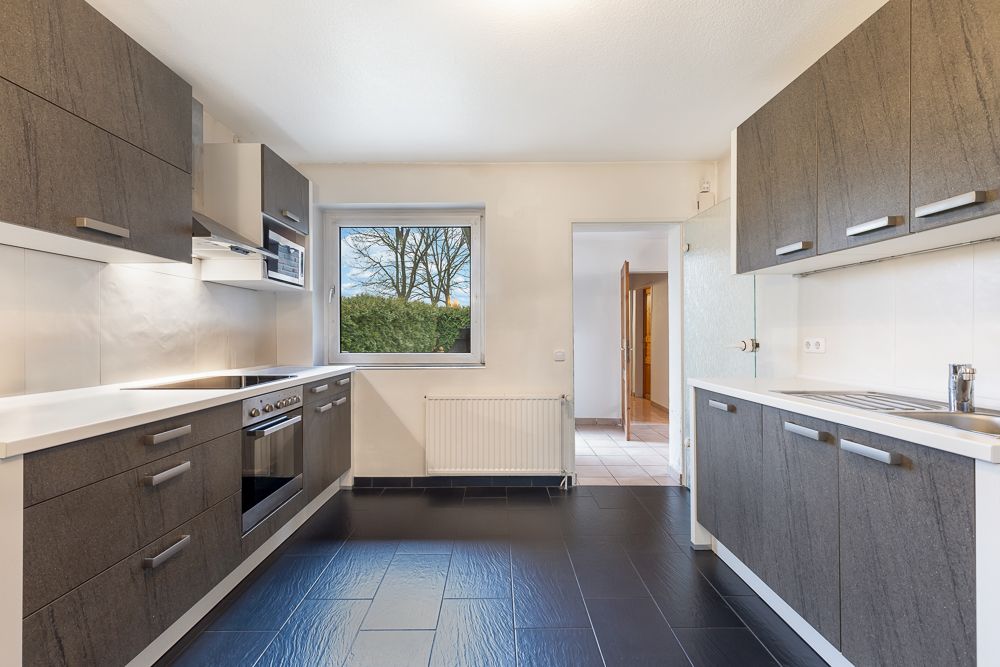 Moderne Einbauküche mit dunklen Schränken, Herd, Spüle und Fenster zum Garten.