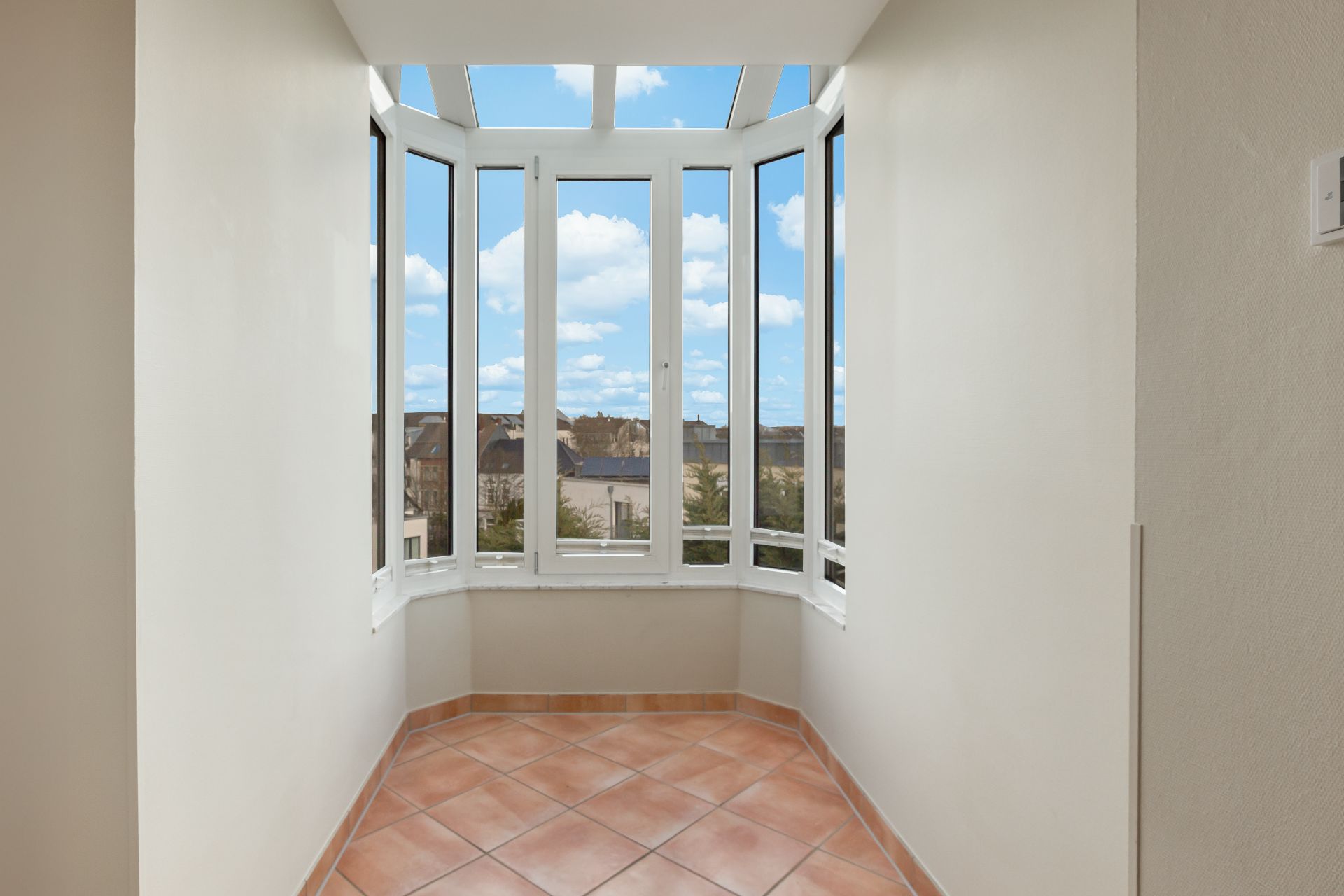 Heller Erker mit großen Fenstern und Fliesenboden, Blick auf Stadt und Himmel.