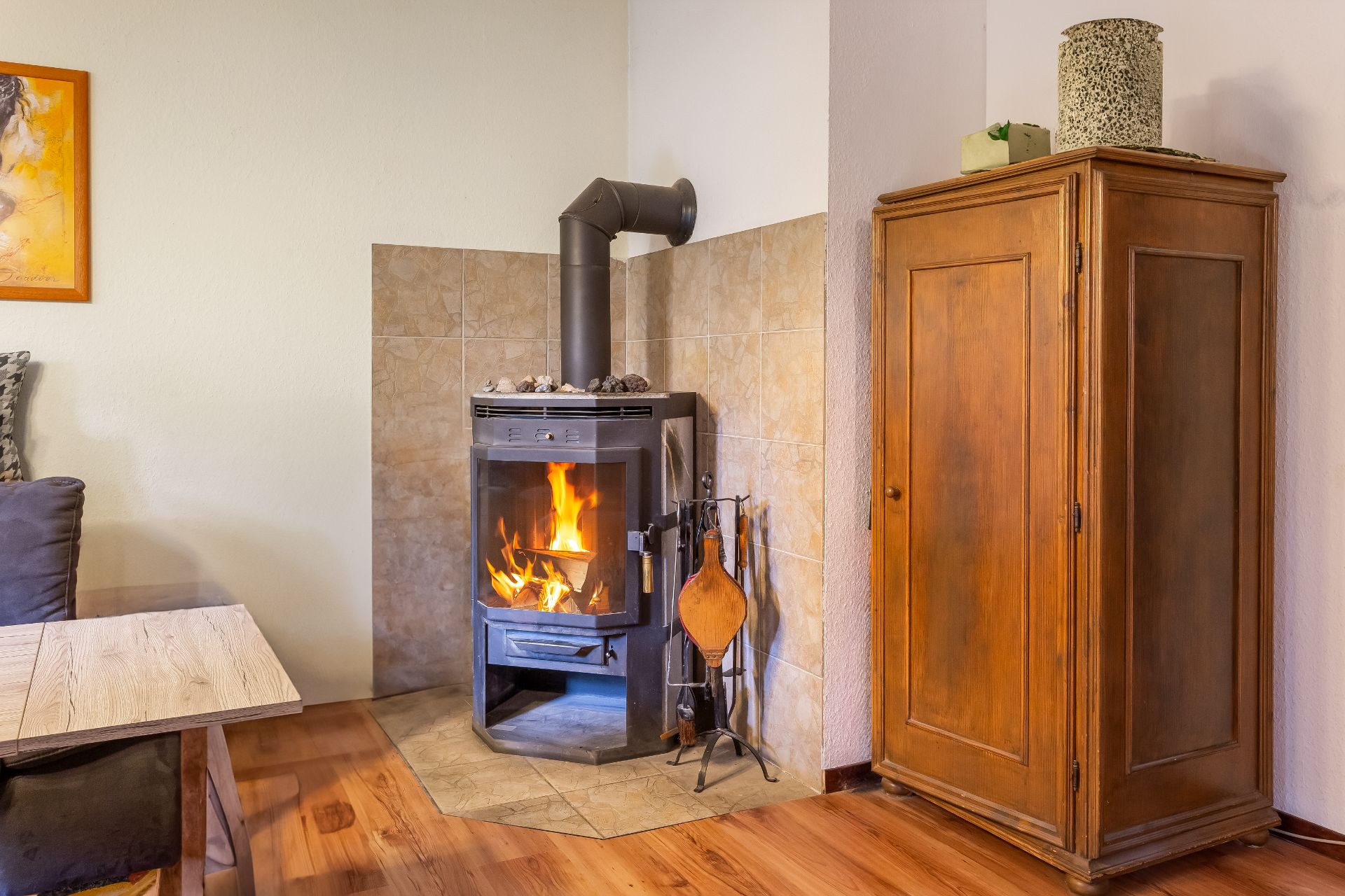 Wohnzimmer mit brennendem Kaminofen, Holzschrank und Couchtisch auf Holzboden.