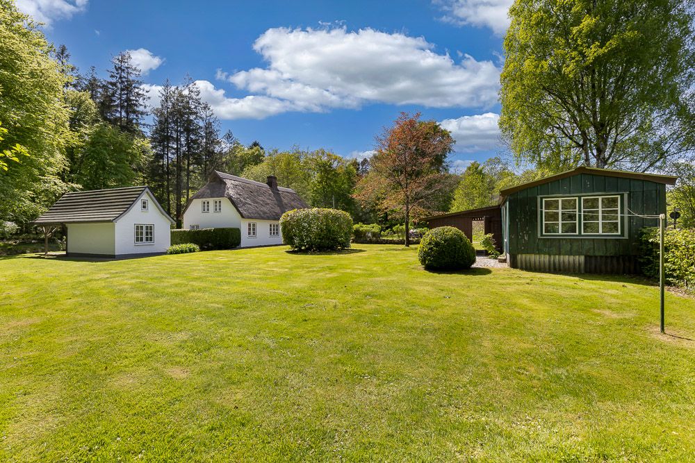 Großer grüner Garten mit drei kleinen Häusern, Bäumen und Sträuchern unter blauem Himmel.