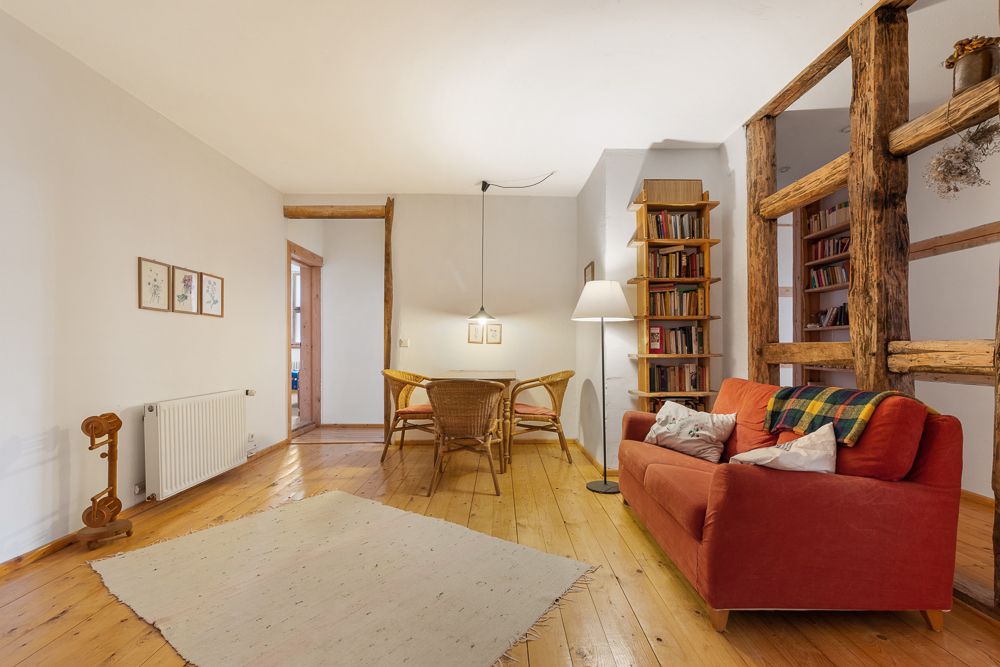 Wohnzimmer mit rotem Sofa, Teppich, Esstisch mit Stühlen, Bücherregal und Holzbalken.