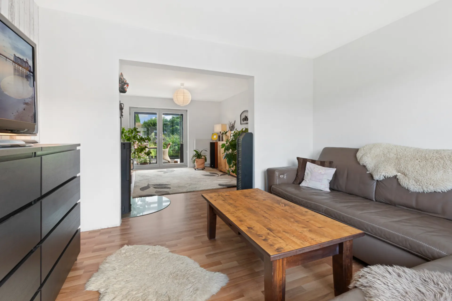 Wohnzimmer mit braunem Ledersofa, Holztisch und Blick auf einen hellen Raum mit Terrassentür.