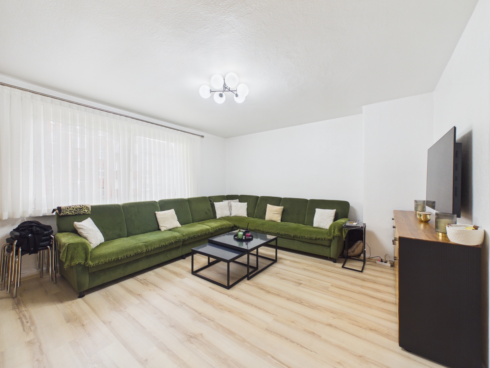 Wohnzimmer mit grünem Ecksofa, Couchtisch, Fernseher und hellem Holzboden.