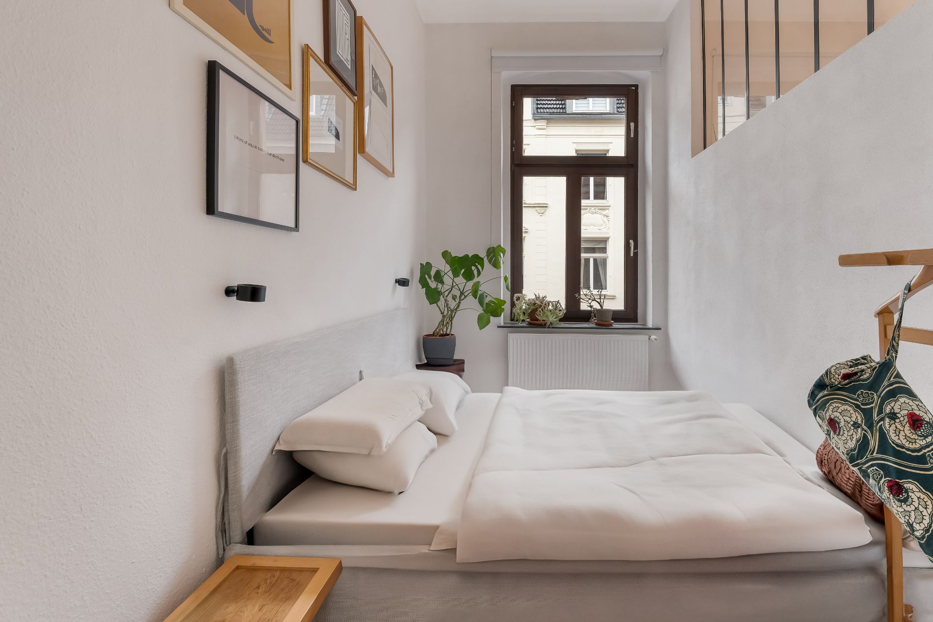Kleines Schlafzimmer mit Doppelbett, Bildern an der Wand und Pflanzen am Fenster.