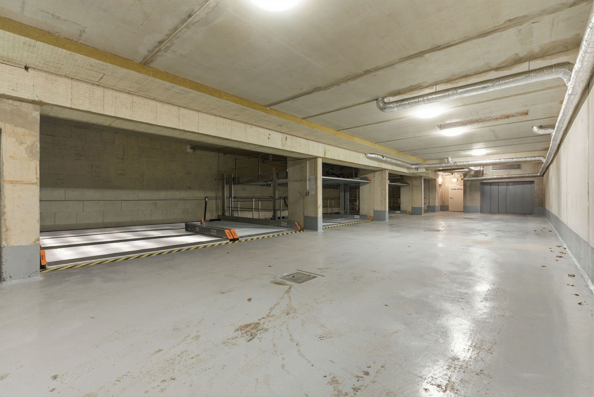 Leerer, gut beleuchteter Tiefgaragenbereich mit mehreren Parkplätzen und Betonwänden.