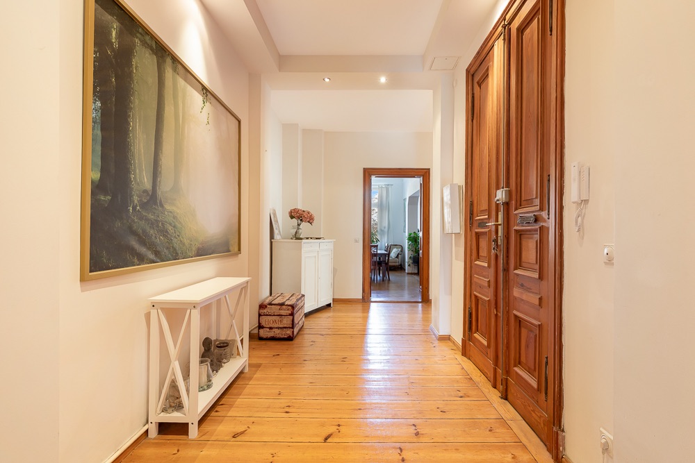 Heller Flur mit Holzboden, großem Wandbild und Holztüren, Blick in angrenzendes Zimmer.
