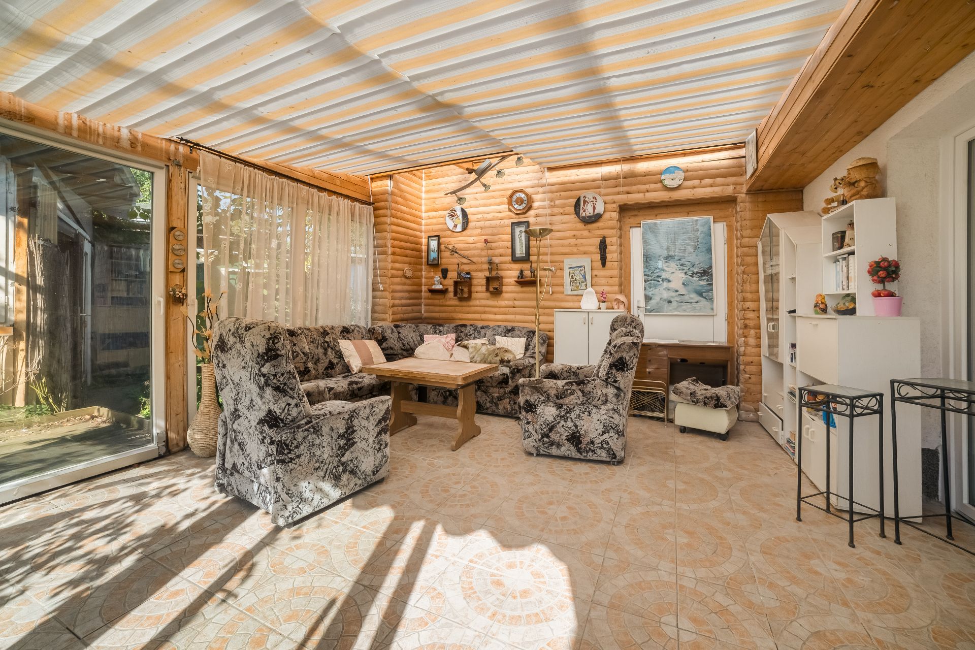 Wintergarten mit gemusterten Sofas, Holztisch, Wanddekoration und Glas-Schiebetür.