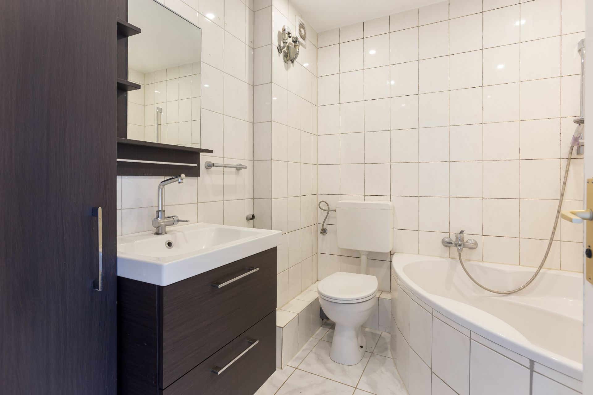 Modernes Badezimmer mit Badewanne, WC, Waschbecken und dunklem Waschtisch.