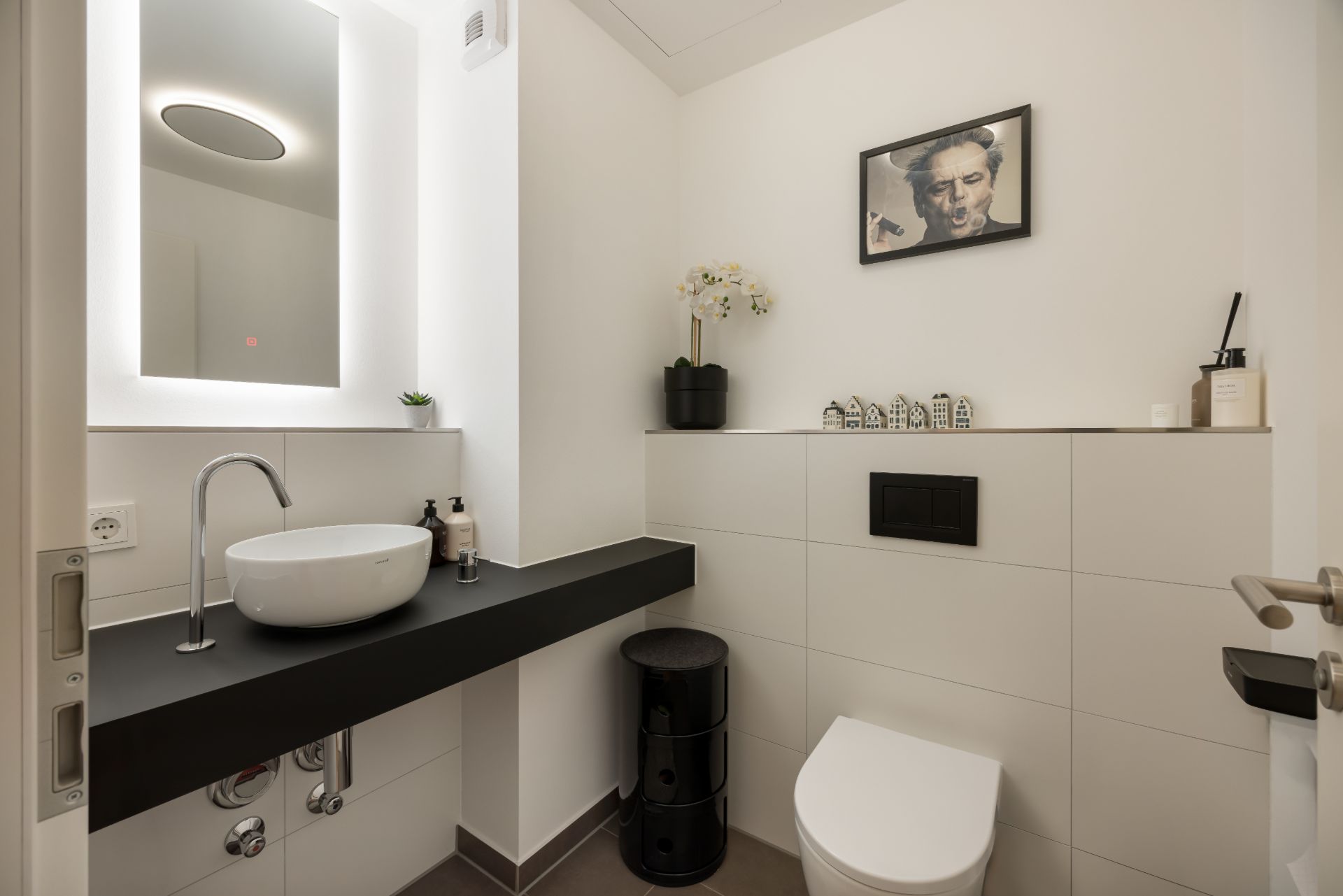 Modernes Badezimmer mit Waschbecken, WC, Spiegel und Dekorationen auf einem weißen Regal.