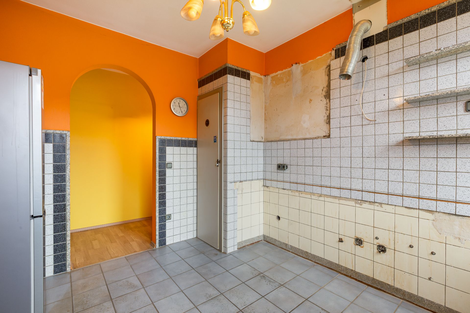Leere Küche mit orangefarbenen Wänden, Fliesenboden und offenen weißen Wandfliesen.