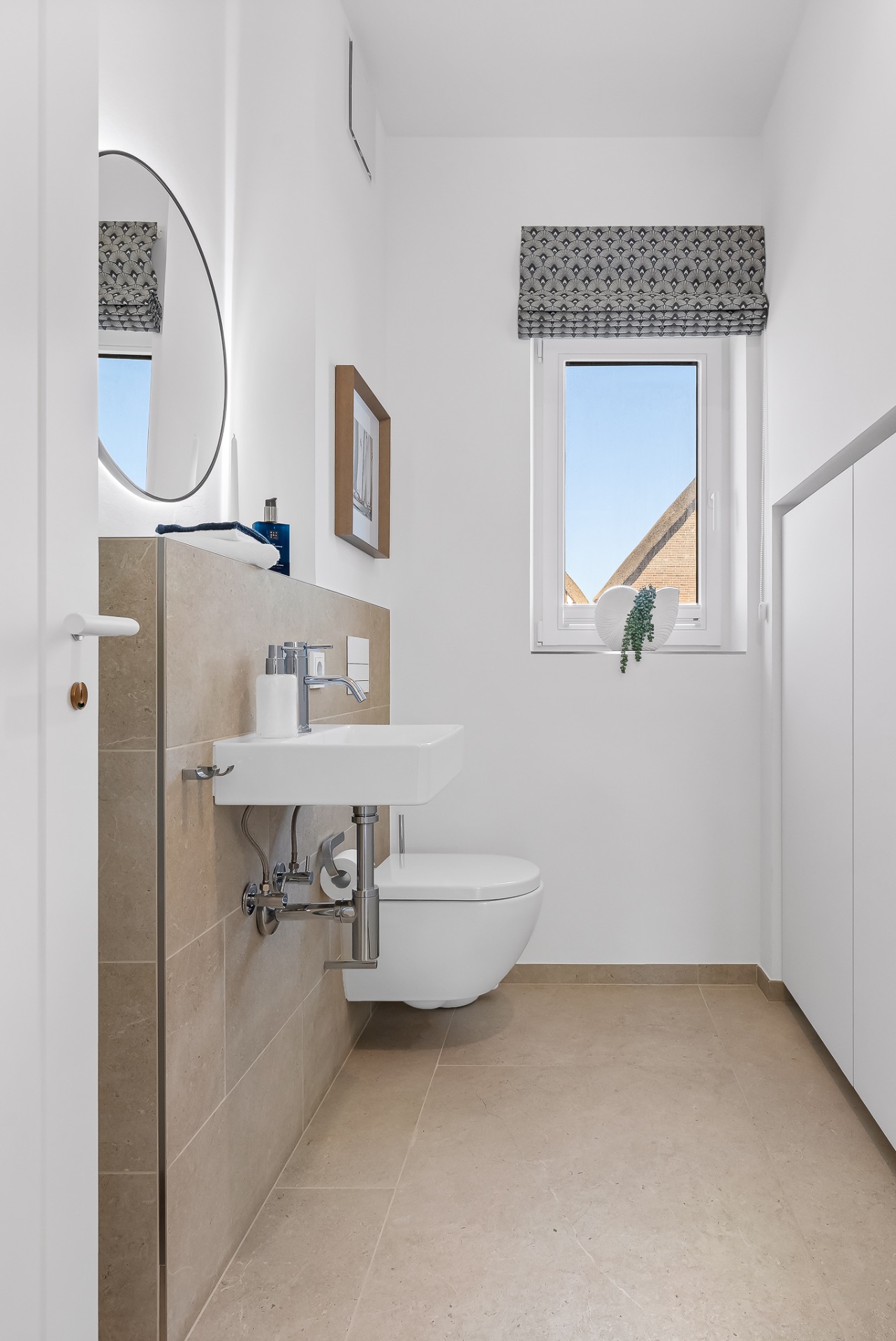 Modernes Badezimmer mit Wand-WC, kleinem Waschbecken, Spiegel und Fenster mit Rollladen.