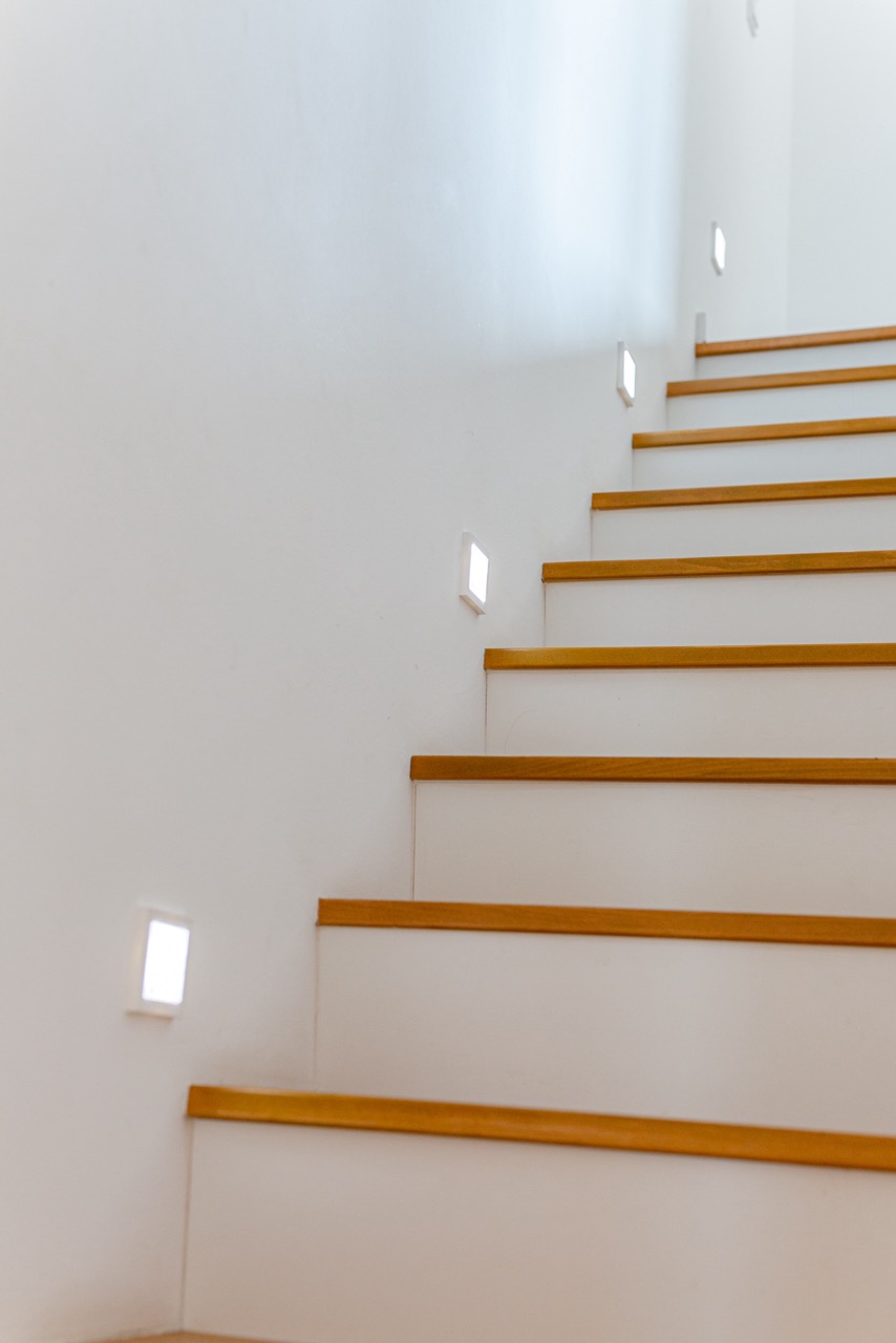 Weiße Treppe mit Holzstufen und kleinen Wandlichtern entlang der Wand.
