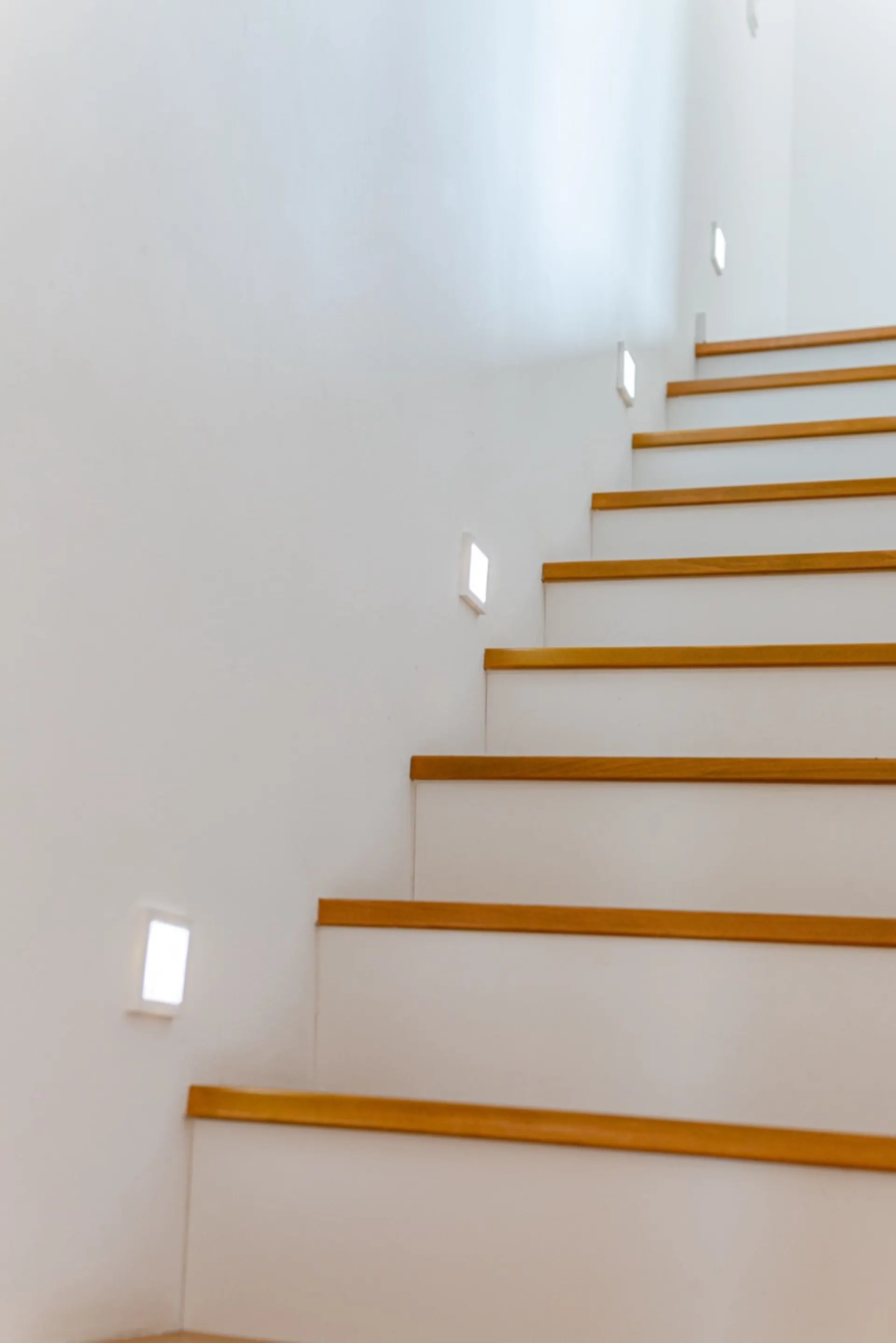Weiße Treppe mit Holzstufen und kleinen Wandlichtern entlang der Wand.