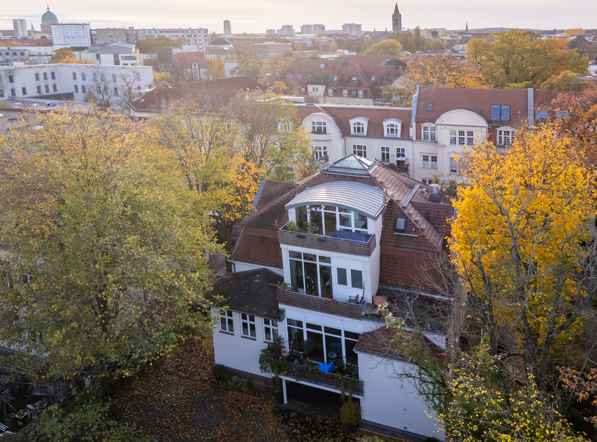 Mehrstöckiges Wohnhaus mit Balkon, umgeben von herbstlichen Bäumen in einer Wohngegend.